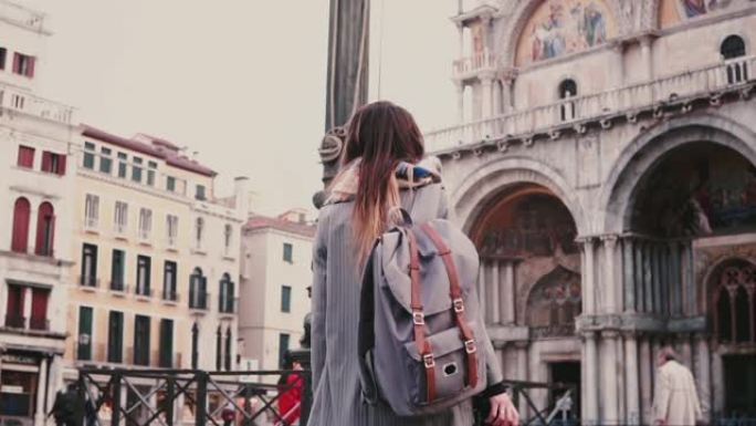 相机跟随时尚的女自由职业者背着背包在威尼斯慢动作拍摄古董老城的照片