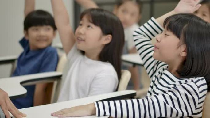 一群快乐的亚洲小学生举起手臂回答教室老师的问题。幼儿园学前概念。