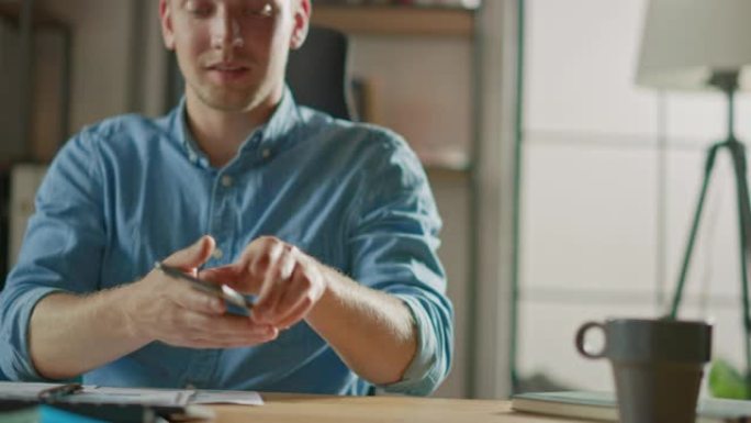 坐在办公桌前的创意企业家在时尚办公室的台式计算机上工作，拿起并开始使用智能手机，使用社交媒体应用程序