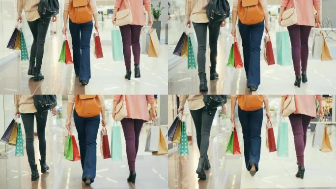 穿着牛仔裤的女性腿的后视图走在购物中心，女孩们背着明亮的纸袋购买。顾客，买东西和休闲概念。