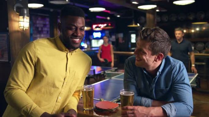 男性朋友在酒吧见面喝酒，顾客在后面打乒乓球