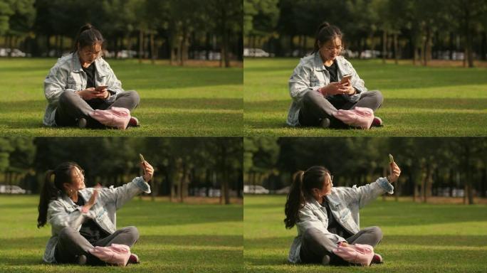 亚洲大学女生坐在草坪上使用手机在校园