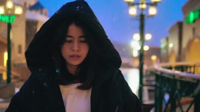开朗的亚洲女人晚上站在雪地里看着相机。