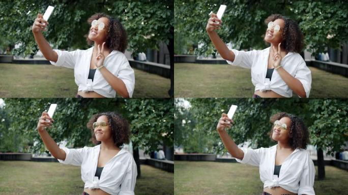 非裔美国女孩在城市公园用智能手机自拍的肖像。