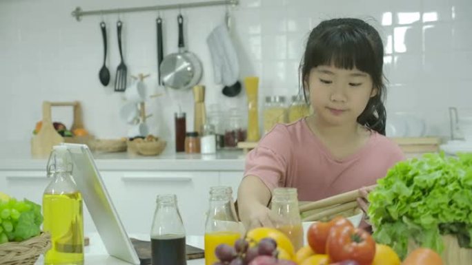 亚洲小女孩在家里的厨房做饭时，在数字平板电脑上寻找沙拉食谱。