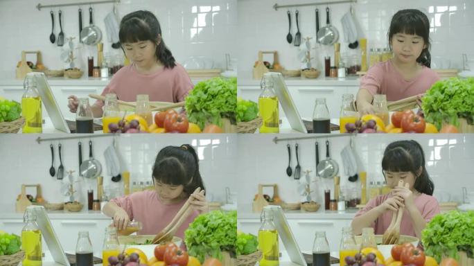 亚洲小女孩在家里的厨房做饭时，在数字平板电脑上寻找沙拉食谱。