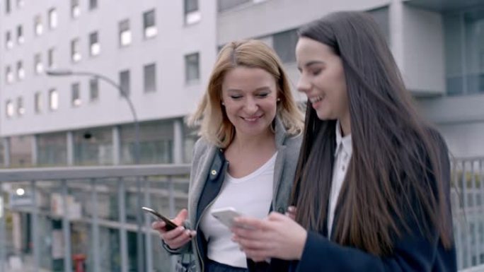 女士快乐的年轻女商人朋友在城市散步和使用智能手机