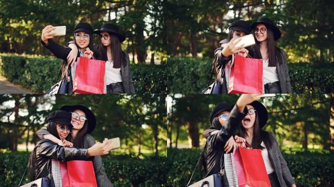 迷人的亚洲女孩在购物后拿着包和使用智能手机与她的白人朋友自拍。现代生活方式、科技与青年观念。