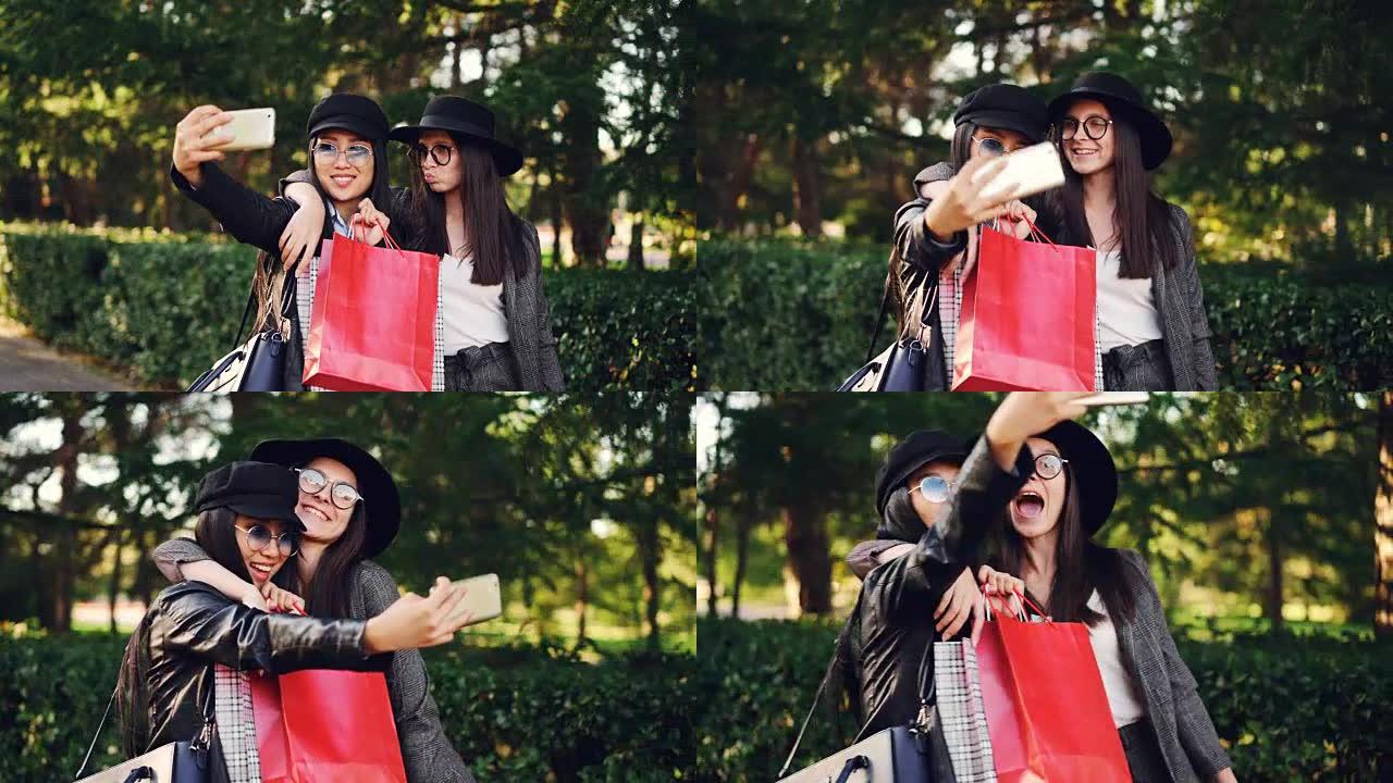 迷人的亚洲女孩在购物后拿着包和使用智能手机与她的白人朋友自拍。现代生活方式、科技与青年观念。