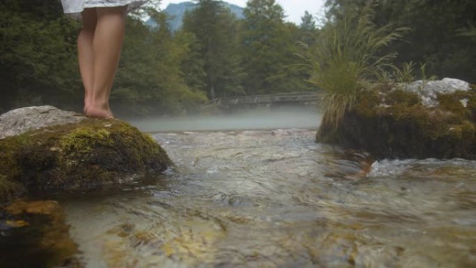 SLO MO赤脚女人站在河里的一块岩石上