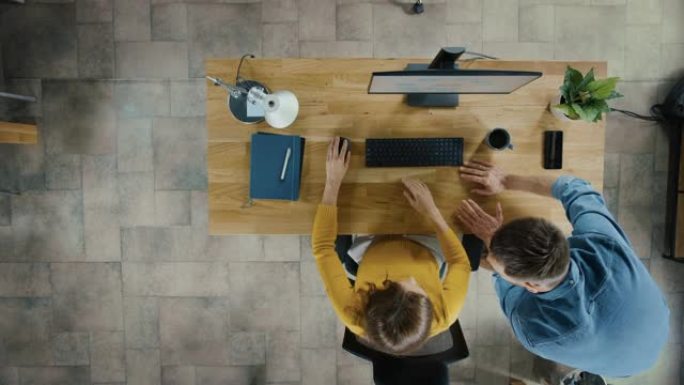 俯视图摄像头拍摄: 女上班族使用台式电脑，项目经理站在旁边，为客户体验管理提供优化工作流程的建议。逐
