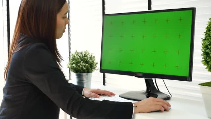 女商人在现代办公室中使用带有绿屏的计算机