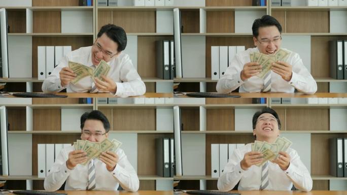 成功的亚洲人的慢动作肖像使金钱高兴。享受美元的经理。职员嗅新的钱。慢动作。