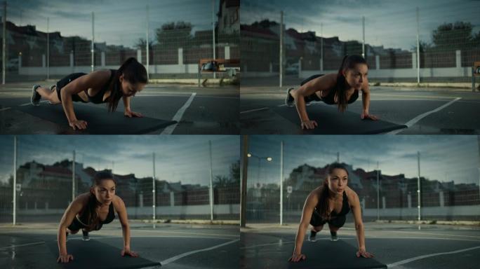 美丽精力充沛的健身女孩做俯卧撑运动。她正在一个有围栏的室外篮球场里锻炼身体。居民区下雨后的晚间录像。