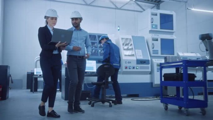 女总工程师和男项目经理走过现代工厂，拿着笔记本电脑，交谈和计划生产的优化。带数控机械和机器人手臂的工