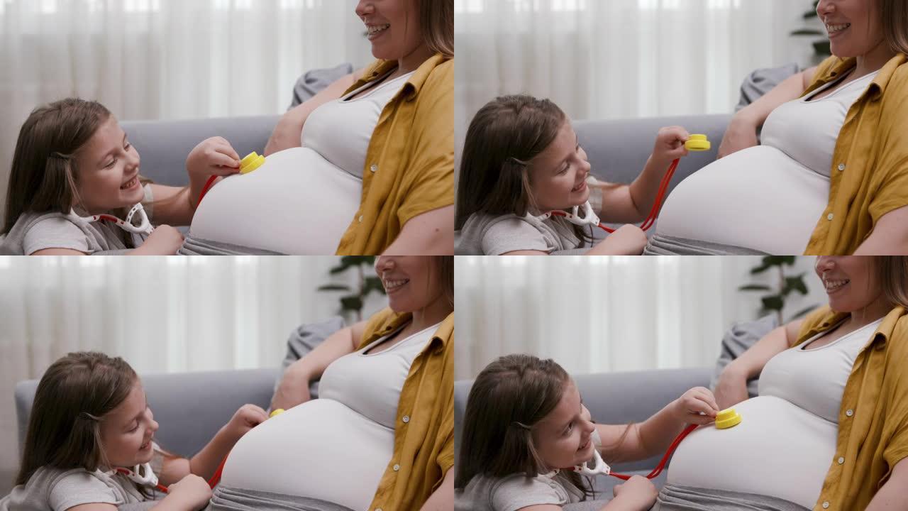 可爱的小女孩和怀孕的女性在医生那里玩。可爱的高加索女儿用玩具医疗设备检查怀孕的妈妈肚子。迷人的孩子和