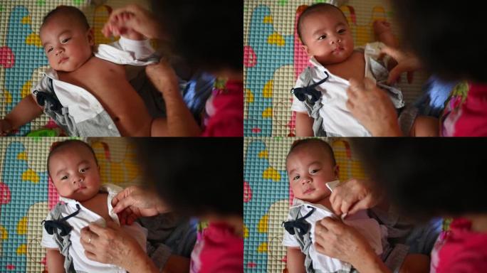 一位亚洲华人祖母在垫子上洗澡后为她5个月大的男婴孙子换衣服