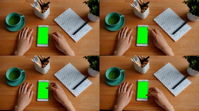女孩的手触摸木制桌子上的绿色色度键智能手机屏幕