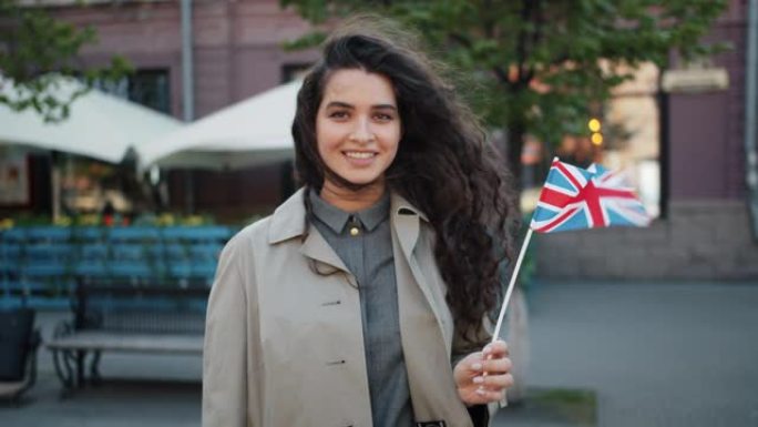 在大风天，快乐的女孩站在户外，带着英国国旗微笑的肖像