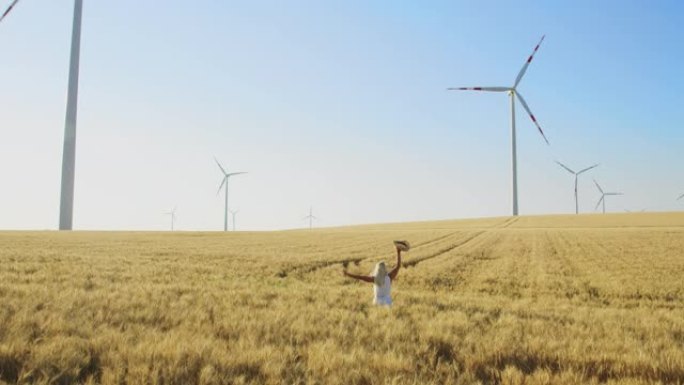 CS快乐的女人在被风力涡轮机包围的麦田中间奔跑