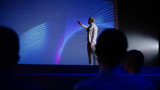 在舞台上，演讲者向观众致意，新产品的演示，使用遥控器进行演示，在大屏幕上显示信息图表，统计动画。实时