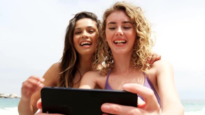 两个混血女性朋友在沙滩上用手机自拍的前视图4k