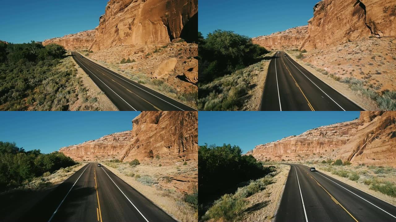 无人机跟随银色汽车在大陡峭的峡谷落基山，茂密的沙漠绿化和树木之间的高速公路上行驶。