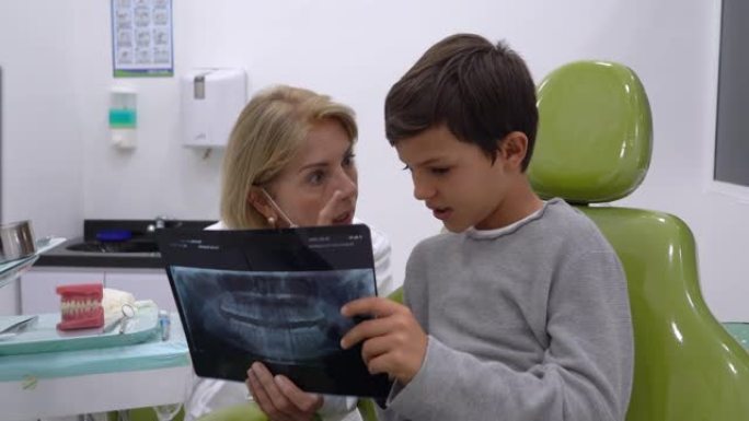 可爱的牙齿科医生向年轻患者解释一些东西，同时向他展示他牙齿的x射线