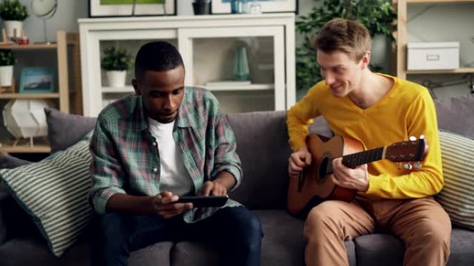 两个男性朋友正在家里学习用平板电脑弹吉他。