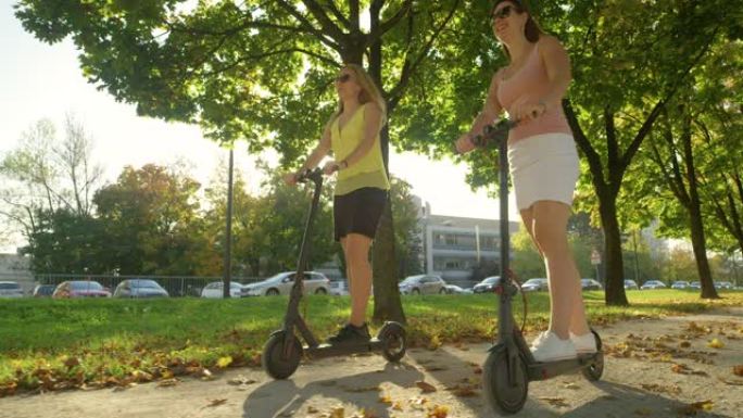 低角度: 微笑的女性在公园里骑着电动滑板车享受阳光明媚的一天