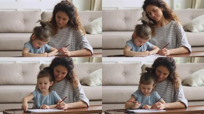 微笑的母亲在家里用铅笔帮助小女儿画画
