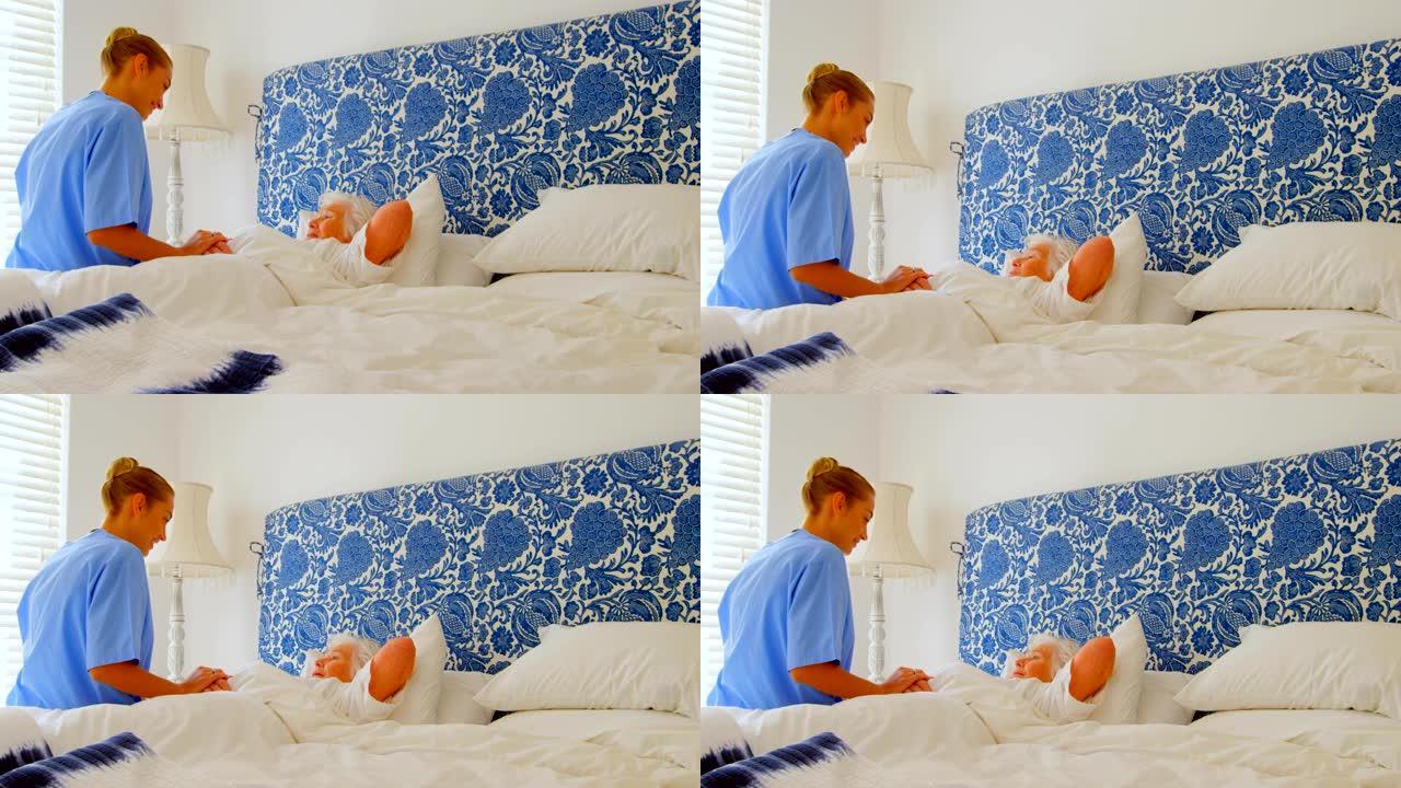 在舒适的家庭4k中，年轻的高加索女医生在床上握着高级女性的手的侧视图