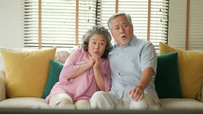 亚洲老年夫妇在客厅里一起激动地看电视电影。人们有放松、老年、退休、老年生活方式的家庭观念。