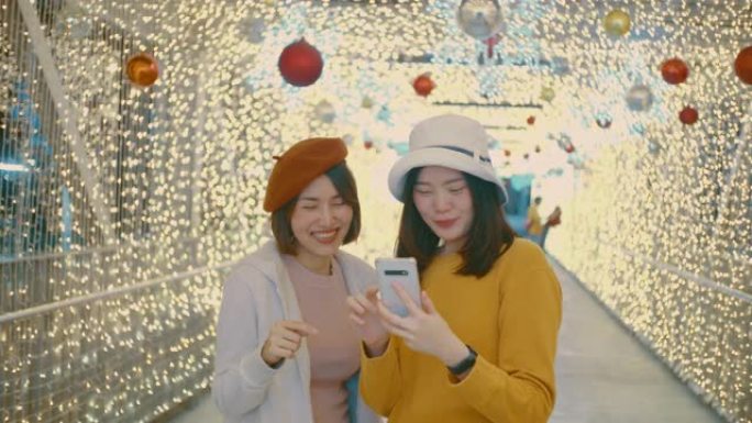 两名年轻女游客在圣诞节用装饰有灯光的手机自拍