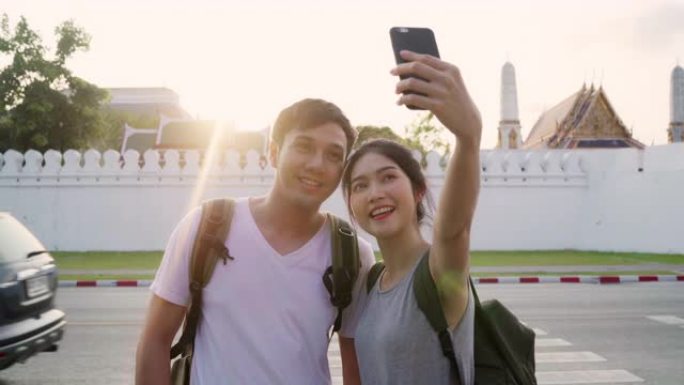 亚洲博主夫妇在泰国曼谷旅行，甜蜜的夫妇使用手机自拍和照片查看，同时在日落的假日旅行中度过甜蜜的时光。