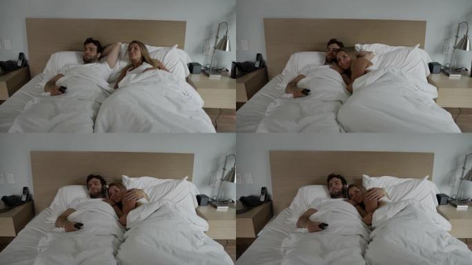 年轻夫妇躺在床上拥抱在一起看电视