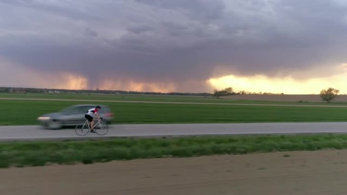 MS男骑车人在乡村道路上骑自行车，背景为暴风云