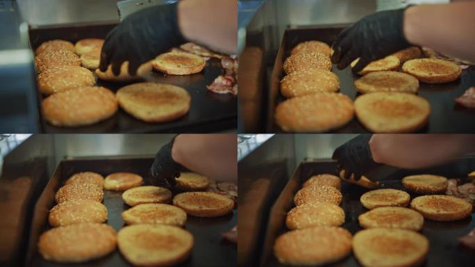 厨师在热气或电炉上用芝麻翻转汉堡面包的美味镜头。正在准备新鲜的美食汉堡。