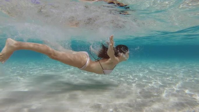 年轻女子的慢动作在假期期间在热带海洋的透明蓝色水中游泳