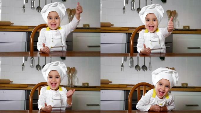一个小女孩在厨房里打扮成专业厨师的肖像，用她的手做ok，作为适当营养和真正食物的标志。