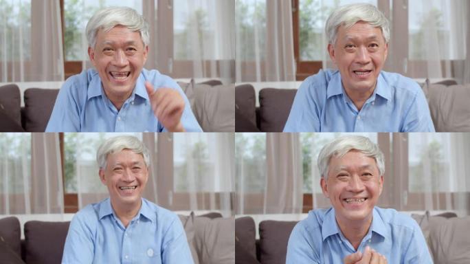 亚洲资深男子在家视频通话。亚洲老年中国男性躺在家里客厅的沙发上，使用手机视频通话与家庭孙子孙女交谈。