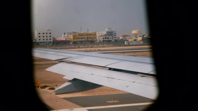 起飞前不久，飞机机翼从靠窗座位上的美丽景色，在阳光明媚的沙漠城市上空飞行。