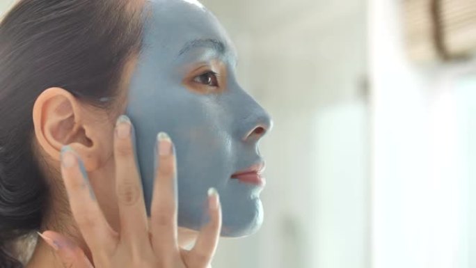亚洲人在家里的浴室里给她脸上戴上蓝色保湿面膜