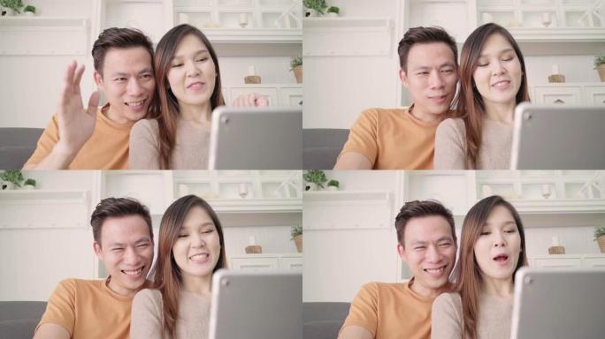 亚洲夫妇在家里的客厅与朋友使用平板视频通话，甜蜜的夫妇在家放松时躺在沙发上享受爱情时刻。生活方式夫妇