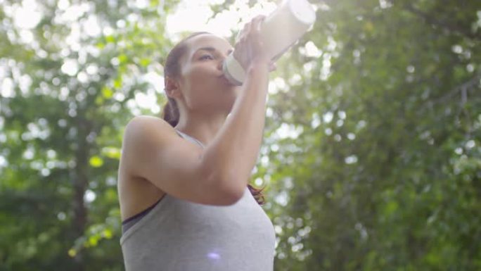 迷人的女运动员在公园锻炼后喝水