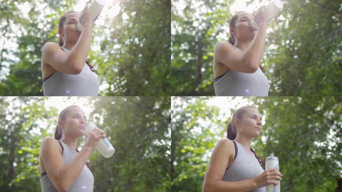 迷人的女运动员在公园锻炼后喝水