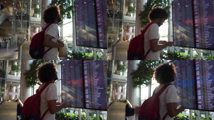 机场的黑人年轻人看着出发时间表屏幕和准备旅行的登机牌
