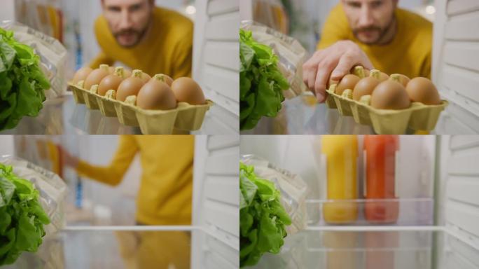 厨房冰箱内的摄像头: 英俊的男人打开冰箱门，里面看着盒装鸡蛋。准备健康餐的人。从装满健康食品和杂货的