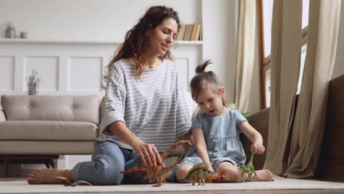 快乐的妈妈带着玩恐龙的小女儿坐在地板上