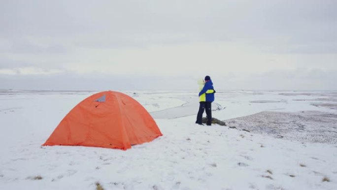 女士深情的夫妇在冰岛偏远的白雪覆盖的景观中拥抱露营帐篷